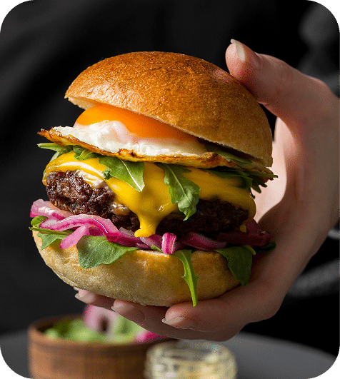 vista frontal persona sosteniendo hamburguesa con huevo frito 1